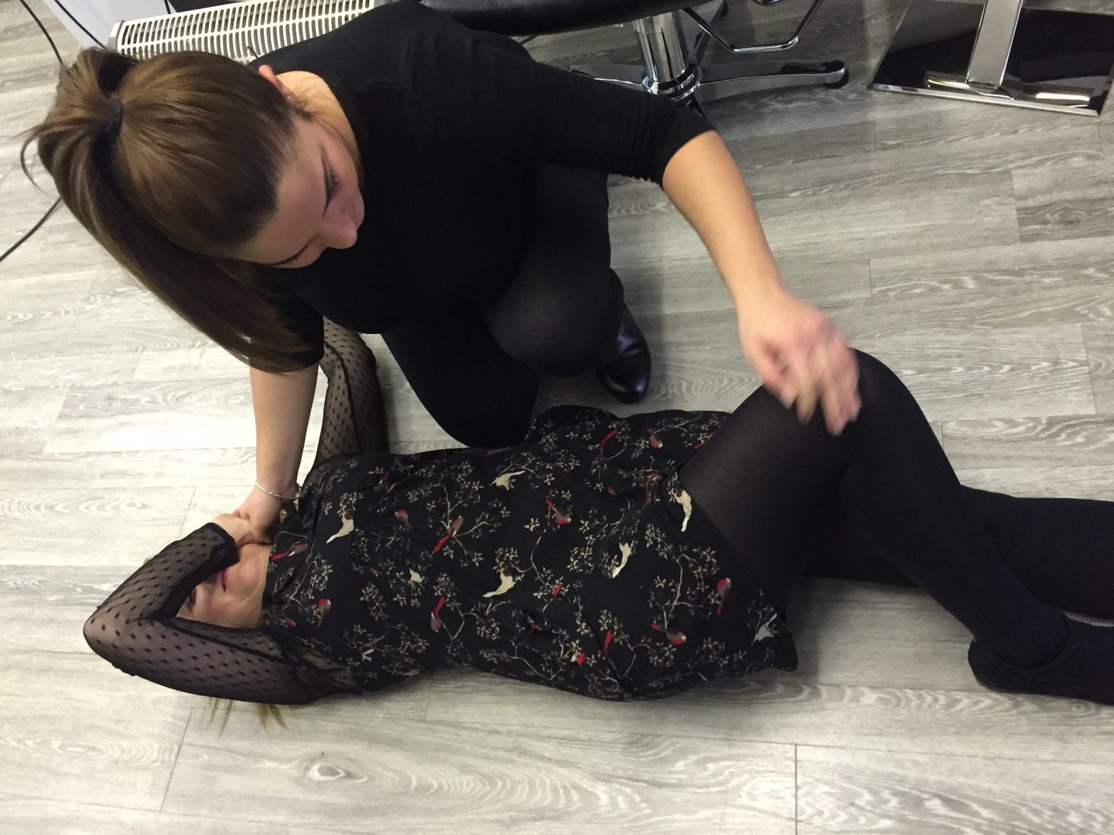 A woman laying on the floor with a woman helping her.